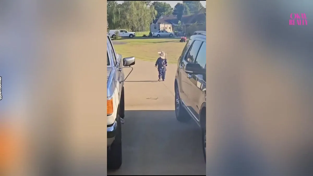 A young boy in a police costume walks toward a house across a front yard